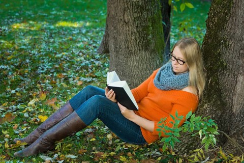 Young woman wearing glasses sitting in the park and reading a book