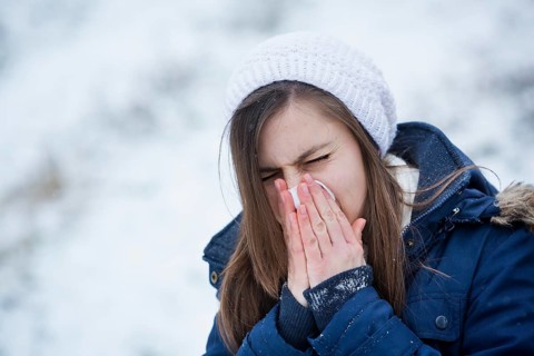 Young woman wearing winter clothes blowing her nose
