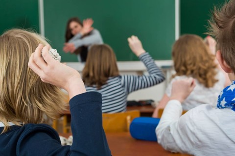 School children in a classroom throwing paper balls at the teacher