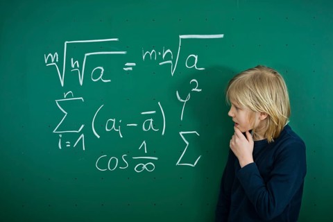 Schoolboy pondering a mathematical formula on a school blackboard