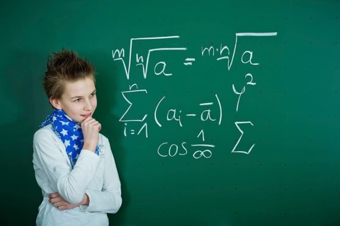 Schoolboy pondering a mathematical formula on a school blackboard