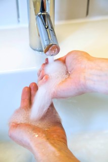 Person washing their hands under running water from a faucet