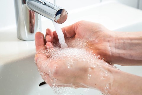 Person washing their hands under running water from a faucet