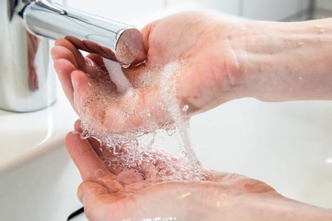Person washing their hands under running water from a faucet