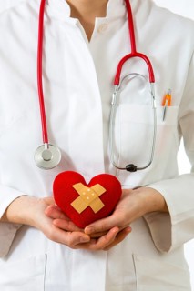 Female doctor holding a red heart with a plaster in her hands