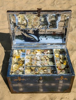 Treasure chest with gold and silver coins on the sand