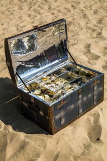 Treasure chest with gold and silver coins on the sand