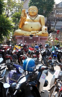 Parking lot for motor scooters in front of a large golden Buddha statue