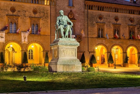 Illuminated Verdi monument in front of Rocca Pallavicino with Opera House Teatro Guiseppe Verdi