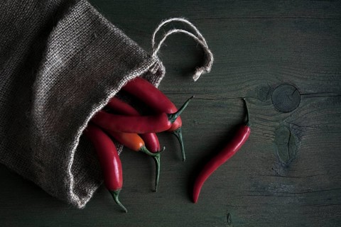 Red peppers in a jute sack lying on a wooden table