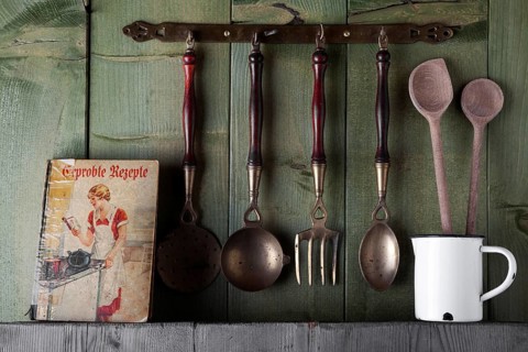 Old cookbook and cooking utensils in front of a green wooden wall