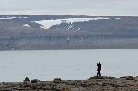 Person with a rifle over their shoulder looking around with binoculars for polar bears