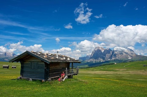 Woman sitting at an alpine hut in front of Piatto Mountain and Sasso Lungo Mountains