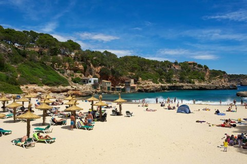 Tourists on the beach in the bay at Cala Llombards