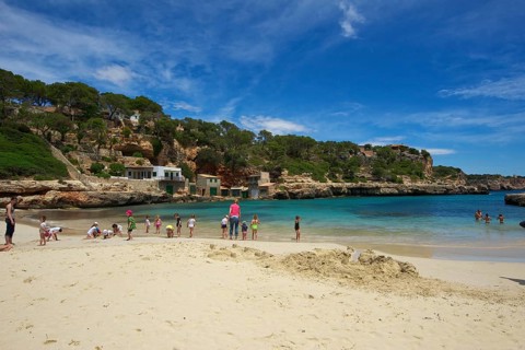 Tourists on the beach in the bay at Cala Llombards