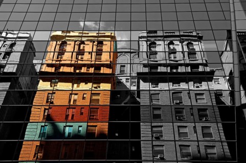Houses are reflected in the glass facade of a skyscraper