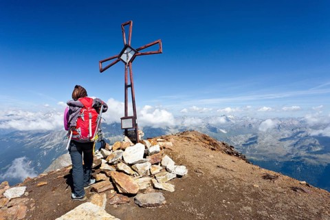 Mountain climber at the summit cross on Schneebiger Nock Mountain in the Rieserferner Group