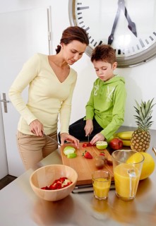 Mother and son cutting various kinds of fruit on cutting board in a kitchen