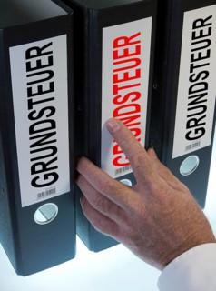 Hand reaching for file folders labeled 'Grundsteuer'