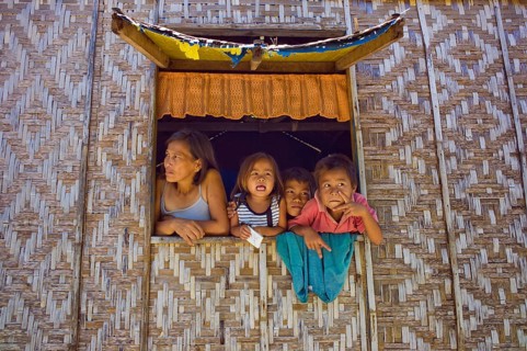 Filipino mother and children looking out of a window of their home