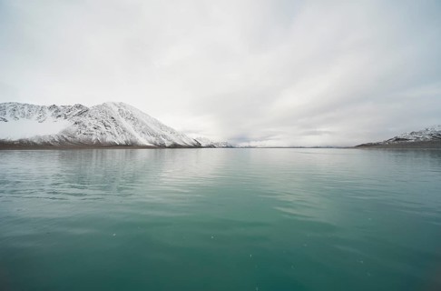 Turquoise-coloured sea in front of snow-covered mountains