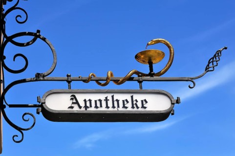 Hanging sign of St. George Apotheke pharmacy against a blue sky