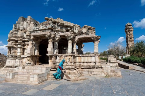 Woman sweeping the stone slabs in front of temple ruins