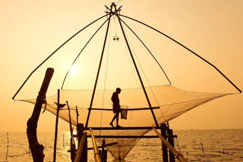 Fisherman holding a landing net in a Chinese fishing net at sunrise