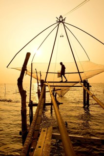 Fisherman holding a landing net in a Chinese fishing net at sunrise