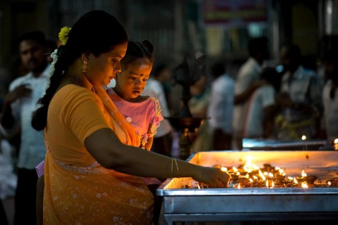Woman holding a child in her arms while lighting oil lamps in a temple