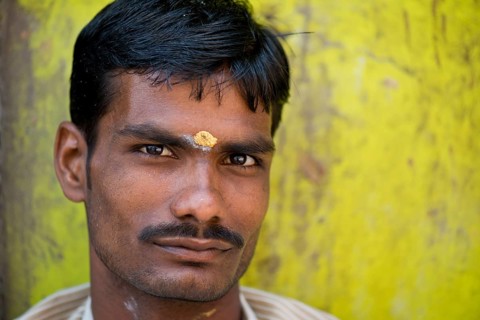Man in front of lemon-yellow wall with bindi on his forehead