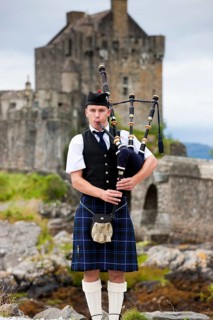 Bagpiper standing in front of Eilean Donan Castle