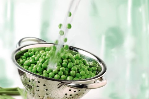 Garden peas and water splashing into a colander