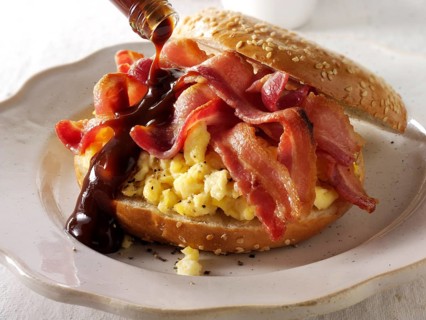 Crispy streaky bacon and scrambled eggs on a bagel with brown sauce