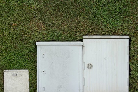 Electrical boxes and Telekom switch boxes in front of a freshly-cut hedge (Thuja)