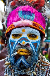 Man in a colourfully decorated costume with face paint and a cigarette at the traditional sing-sing gathering