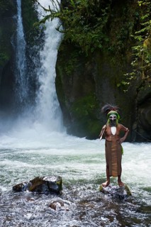 Decorated and painted tribal chief standing in front of a waterfall in the Highlands
