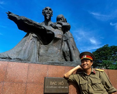 Soldier leaning against the statue of Ho Chi Minh or 'Uncle Ho' with a child