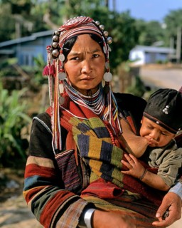 Woman from the people of the Akha wearing traditional costume while nursing a boy