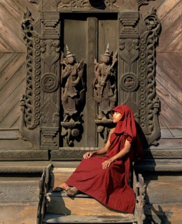 Monk sitting in front of a carved teak door