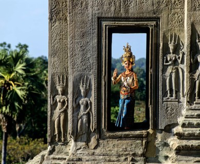 Temple dancer or apsara in a window of the temple of Angkor Wat beside apsara reliefs