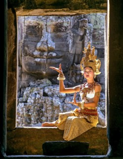 Temple dancer or apsara sitting in a window in front of a face tower at Bayon Temple