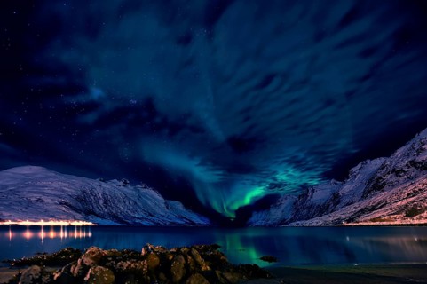 Aurora over a fjord with snow-covered mountains and an illuminated village