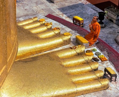Monk praying at the feet of the golden Buddha statue of Wat Intharawihan