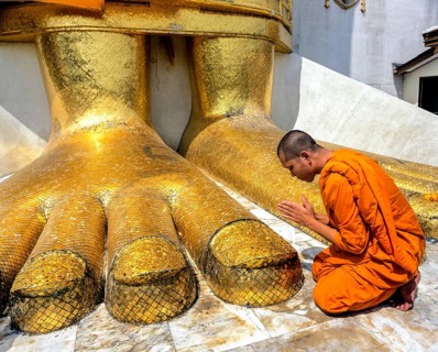 Monk praying at the feet of the golden Buddha statue of Wat Intharawihan