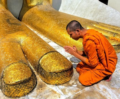 Monk praying at the feet of the golden Buddha statue of Wat Intharawihan