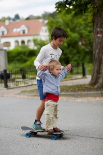 Older and younger brothers riding a skateboard