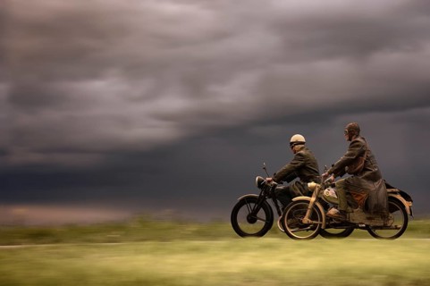 Two vintage motorcyclists in front of a dramatic cloudy sky