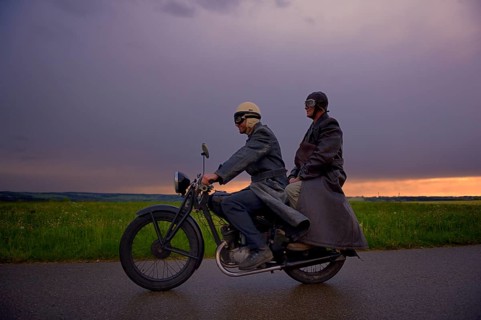 Two vintage motorcyclists in front of a dramatic cloudy sky