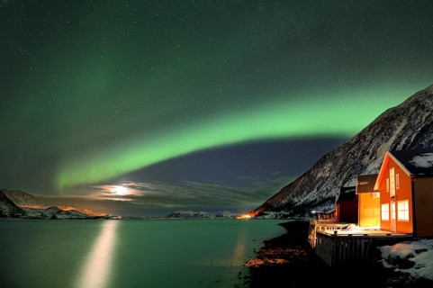 Red fishing huts on the fjord in winter with Northern Lights